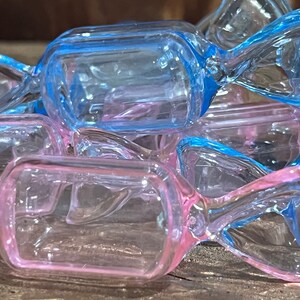 May include: A group of clear plastic candy containers in blue and pink. The containers are shaped like a candy with a twist at the top.