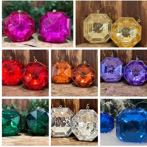 May include: A selection of faceted Christmas baubles in vibrant colours: pink, yellow, red, orange, purple, green, silver, and blue. Each bauble has a gold hanging string and a geometric design. The baubles are for festive decoration.