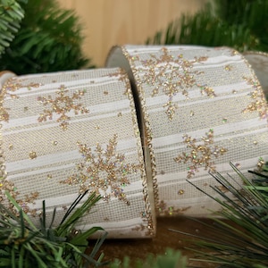 May include: White and gold ribbon with a snowflake pattern and glitter. The ribbon has white stripes and gold snowflakes with glitter.