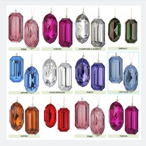 Op de afbeelding: Assortiment van facetgeslepen kristallen ornamenten in diverse kleuren, waaronder roze, fuchsia, helder, smaragd, saffier, paars en lichtblauw. Elk ornament is opgehangen aan een dun gouden draadje. Kleurnamen zijn zichtbaar.