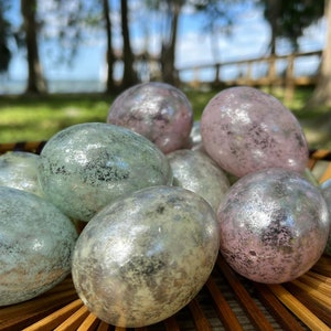 May include: A collection of iridescent Easter eggs in a woven basket. The eggs are a mix of light blue and pink with a shimmery finish.