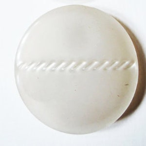 May include: A round, off-white button with a textured, twisted rope design across the center. The button has a smooth, glossy finish and is set against a white background. This button is suitable for sewing projects.