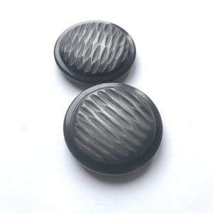 Könnte beinhalten: Zwei dunkelgraue, runde Knöpfe mit einem strukturierten, diagonalen Muster. Die Knöpfe sind vor einem weißen Hintergrund platziert, was ihr detailliertes Design und ihre Farbe hervorhebt.