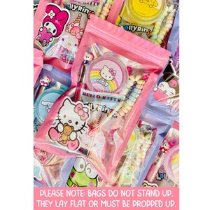 May include: Pink zippered bags filled with colorful candies and Hello Kitty-themed treats. The bags contain lollipops, stickers, and other sweets. The image includes text that reads "PLEASE NOTE: BAGS DO NOT STAND UP. THEY LAY FLAT OR MUST BE PROPPED UP."