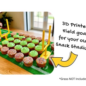 May include: Cupcakes arranged on a green surface to resemble a football field, with green frosting and sprinkles. Yellow 3D-printed field goal posts are placed on the field. Text reads: "3D Printed Field goals for your own Snack Stadium!" The grass is not included.