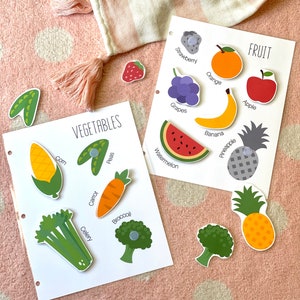 Pu&ograve; includere: Due carte bianche con immagini colorate di frutta e verdura. La carta superiore ha la parola "FRUTTA" e immagini di fragola, arancia, mela, banana, ananas e uva. La carta inferiore ha la parola "VERDURA" e immagini di mais, piselli, carota, sedano, broccoli e anguria.