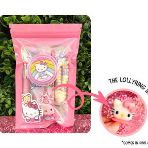 May include: A pink cellophane bag filled with Hello Kitty themed items. The bag contains a pen, stickers, a round container, and candy. A separate image shows a Hello Kitty ring, available in pink or red.