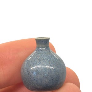 Może przedstawiać: Mały, okrągły, niebieski ceramiczny wazon o nakrapianej fakturze. Wazon ma wąską szyjkę i lekko rozszerzoną krawędź. Ogólny kształt jest pękaty, a kolor to stonowany niebieski z ciemniejszymi plamkami.