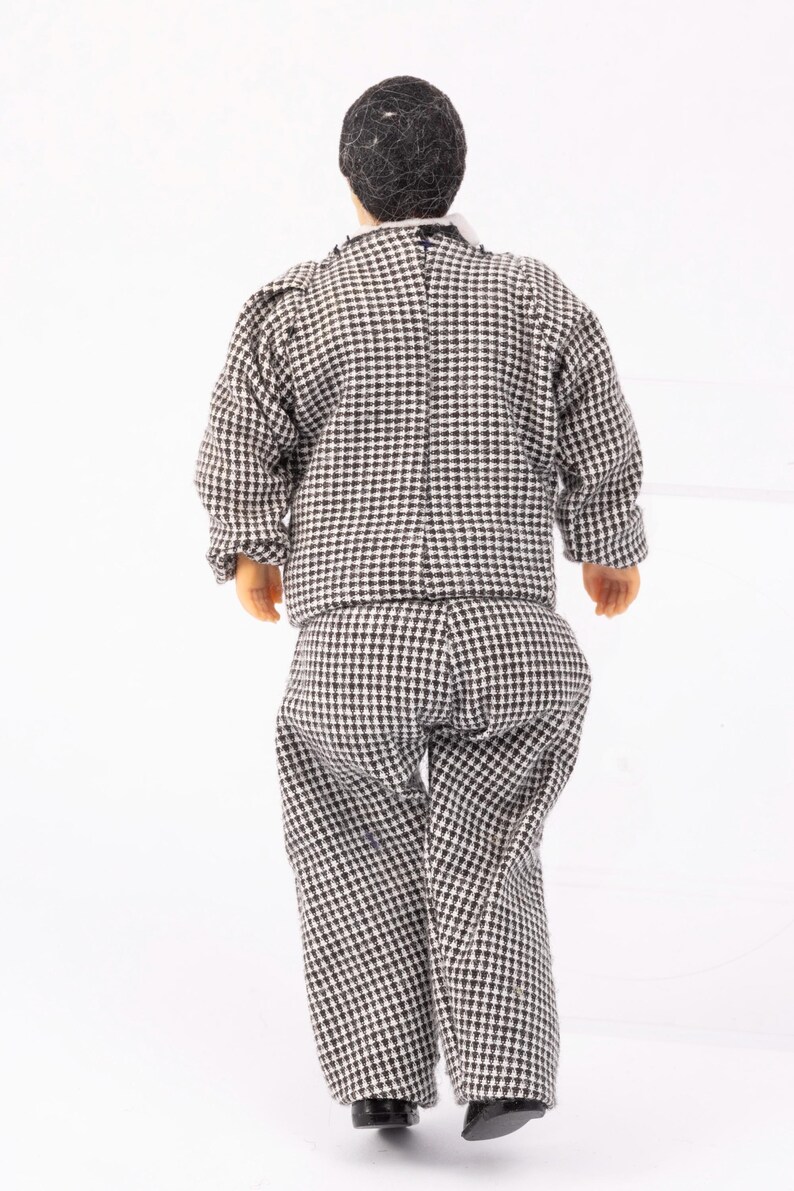 May include: A black and white checkered suit with a black jacket and pants. The suit is worn by a doll with black hair.
