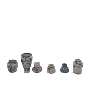 May include: A collection of six miniature ceramic vases in varying shapes and sizes. Each vase is white with blue painted designs, including floral and landscape motifs. The vases are arranged in a row against a white background.
