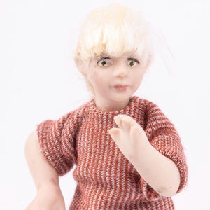 May include: A porcelain doll with blonde hair wearing a red and white striped sweater and blue jeans.