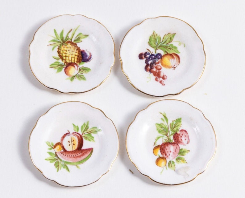 K&ouml;nnte beinhalten: Set aus vier wei&szlig;en Desserttellern aus Keramik mit goldfarbenem Rand. Jeder Teller zeigt ein anderes Fruchtdesign: Ananas, Trauben, Wassermelone und Erdbeeren.