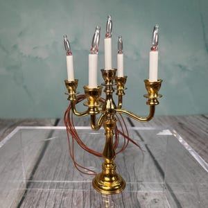 May include: A gold candelabra with five candle holders and clear glass bulbs. The candelabra is on a clear surface.