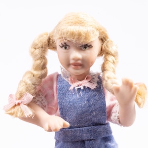 May include: A porcelain doll with blonde braids wearing a pink and blue dress. The doll has a painted face with blue eyes and a pink bow in her hair.