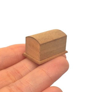 May include: A miniature wooden chest with a curved top and a rectangular base. The chest is made of light-colored wood and appears to be handcrafted. The small size suggests it could be used for decorative purposes or as a dollhouse accessory.