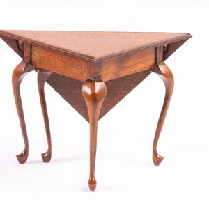May include: A triangular wooden table with a dark brown finish and three cabriole legs. The table is made of solid wood and has a simple, elegant design.