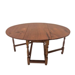 May include: A round, wooden drop-leaf table with a warm brown finish. The table has a circular top and four legs. When the leaves are up, the table is approximately 36 inches in diameter. The legs are connected by a stretcher.