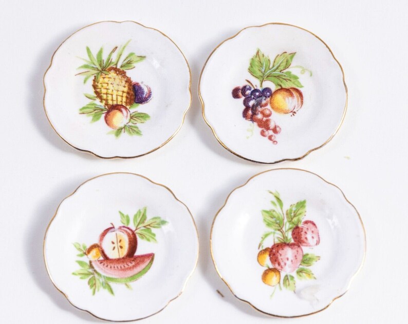 K&ouml;nnte beinhalten: Set aus vier wei&szlig;en Desserttellern aus Keramik mit goldener Verzierung. Jeder Teller zeigt ein anderes Fruchtdesign: Ananas, Trauben, Wassermelone und Erdbeeren.