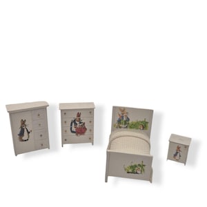 Può includere: Un set da camera in miniatura con letto, cassettiera, armadio e comodino. Ogni pezzo è dipinto di bianco e decorato con illustrazioni di un coniglio. Il letto ha una coperta bianca e una testiera verde.