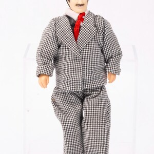 May include: A miniature doll wearing a black and white checkered suit with a red tie. The doll has brown hair and a mustache.