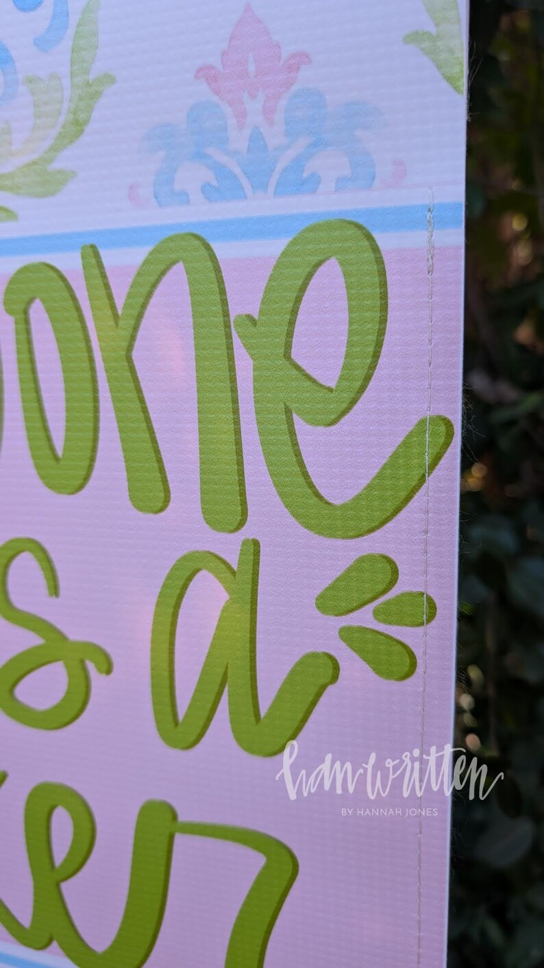 May include: A sign with the words "one is a" in large, lime green script. The background is light pink with a decorative floral pattern in pastel colors. The words "ham written" and "by Hannah Jones" are in the bottom right corner.