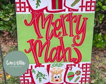 May include: A rectangular garden flag with a green background and red text reading Merry Mahj. The design features white tiles with red borders, numbered 1 through 4, displaying illustrations of mistletoe, a gift, a ball, and a reindeer labeled Joker.