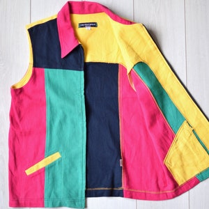 Könnte beinhalten: Eine ärmellose, mit Reißverschluss zu schließende Weste mit Patchwork-Muster in Rot, Grün, Schwarz und Gelb. Die Weste hat einen Kragen und zwei Taschen.