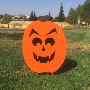 May include: A large orange pumpkin with a carved jack-o'-lantern face. The pumpkin is standing on a green grassy lawn.