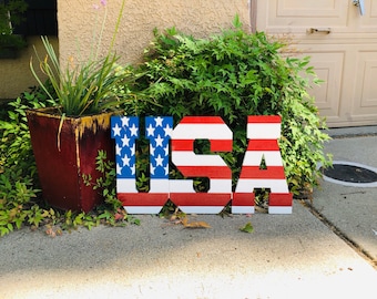 May include: Large wooden letters spelling "USA" painted in red, white, and blue to resemble the American flag.