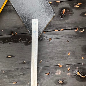 May include: A black and yellow sign with a metal bracket attached to the bottom. The sign is on a wooden surface.