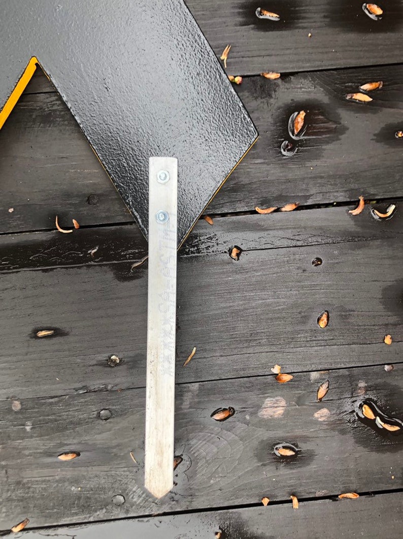 May include: A black and yellow sign with a metal bracket attached to the bottom. The sign is on a wooden surface.