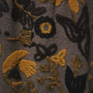 Könnte beinhalten: Nahaufnahme eines braunen Stoffes mit einem strukturierten Muster aus gelben und schwarzen Blumen. Der Stoff hat eine flauschige Textur und ist aus Wolle.