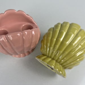 May include: Two ceramic seashell-shaped toothbrush holders. One is pink and the other is green.