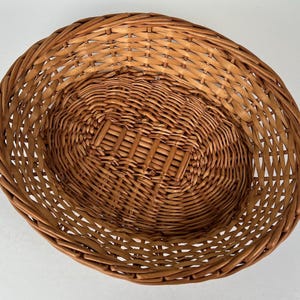 May include: A woven wicker basket with a natural brown color. The basket is oval shaped and has a wide opening.