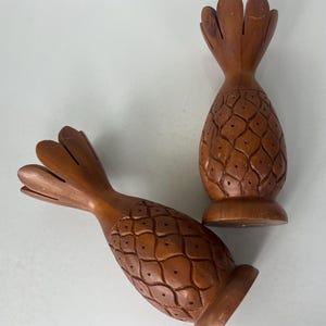 May include: Two wooden pineapple-shaped candle holders. The holders are carved with a pineapple pattern and have a brown finish.