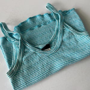Puede incluir: Una camiseta sin mangas a rayas turquesa y blanca doblada con tirantes finos. La parte superior tiene un escote acanalado y est&aacute; hecha de un material suave y ligero. La camiseta sin mangas es una prenda informal para todos los d&iacute;as.