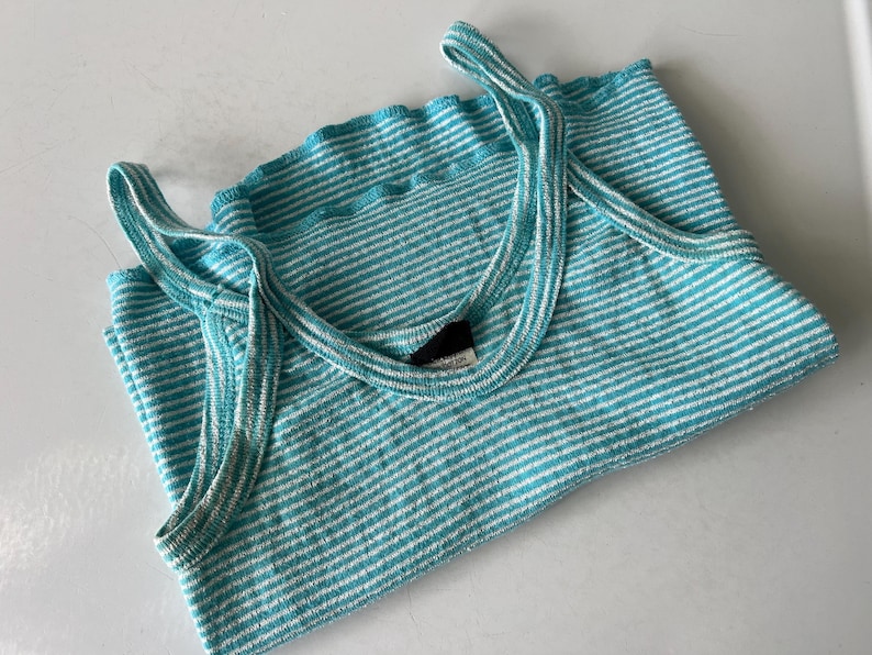 Puede incluir: Una camiseta sin mangas a rayas turquesa y blanca doblada con tirantes finos. La parte superior tiene un escote acanalado y est&aacute; hecha de un material suave y ligero. La camiseta sin mangas es una prenda informal para todos los d&iacute;as.