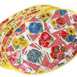 May include: A stack of oval-shaped placemats with a floral design. Each placemat features a patchwork pattern with red and white gingham squares and floral squares. The edges are trimmed with yellow binding.
