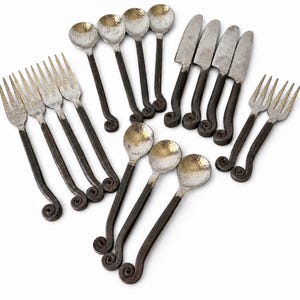 May include: A set of flatware featuring four forks, four spoons, four knives, and two smaller forks. Each piece has a hammered silver-tone metal head and a dark, textured metal handle that terminates in a decorative curled scroll design.