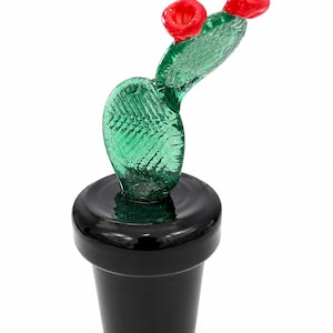 May include: A glass cactus sculpture with a green body and two red flower buds. The cactus is in a black pot. The sculpture is a decorative item.