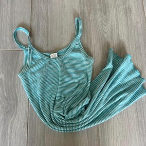 Puede incluir: Vestido de tirantes a rayas turquesa y blancas con tirantes finos. El vestido est&aacute; hecho de tejido de punto acanalado y est&aacute; sobre una superficie de madera.