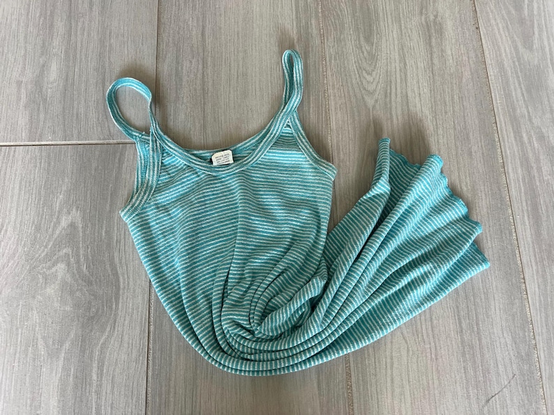 Puede incluir: Vestido de tirantes a rayas turquesa y blancas con tirantes finos. El vestido est&aacute; hecho de tejido de punto acanalado y est&aacute; sobre una superficie de madera.