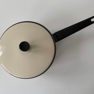 May include: A white ceramic saucepan with a black handle. The saucepan has a black knob on the lid.
