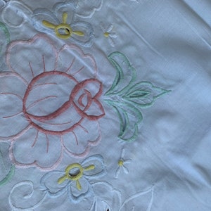 May include: White cotton fabric with embroidered flowers in pink, green, blue, and yellow. The flowers are in a floral pattern.