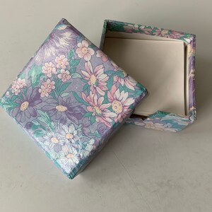 May include: A floral patterned box with a white interior. The box is open and the lid is laying next to it.
