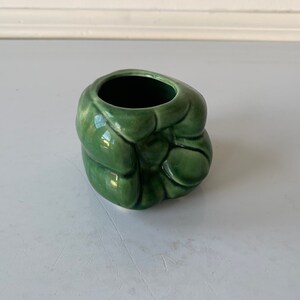 May include: A small, green ceramic planter shaped like a cluster of leaves. The planter has a smooth, glossy finish and a round opening at the top.
