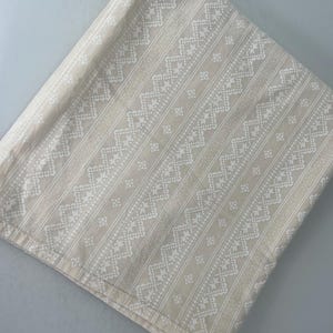 May include: A beige fabric with a white geometric pattern. The pattern is a repeating design of diamonds and stars.