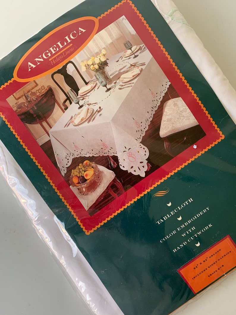 May include: White tablecloth with colour embroidery and hand cutwork. The tablecloth is 163 cm by 213 cm and includes eight napkins. The tablecloth is shown on a table with a centrepiece of fruit and flowers.