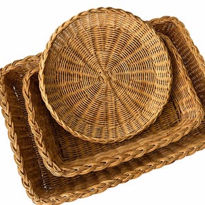 May include: A set of three nested wicker baskets featuring a natural light brown finish. The collection includes two rectangular baskets with braided rims and one circular basket with a woven base, all crafted from thin, flexible plant-based fibers.