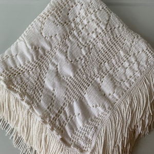 May include: A white crocheted throw blanket with a fringe border. The blanket has a delicate, intricate pattern.